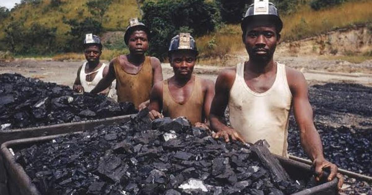 Coal miners with mining helmets standing behind carts filled with coal